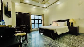 Una habitación de hotel con cama, mesita de noche, lámpara, armario y escritorio con silla.