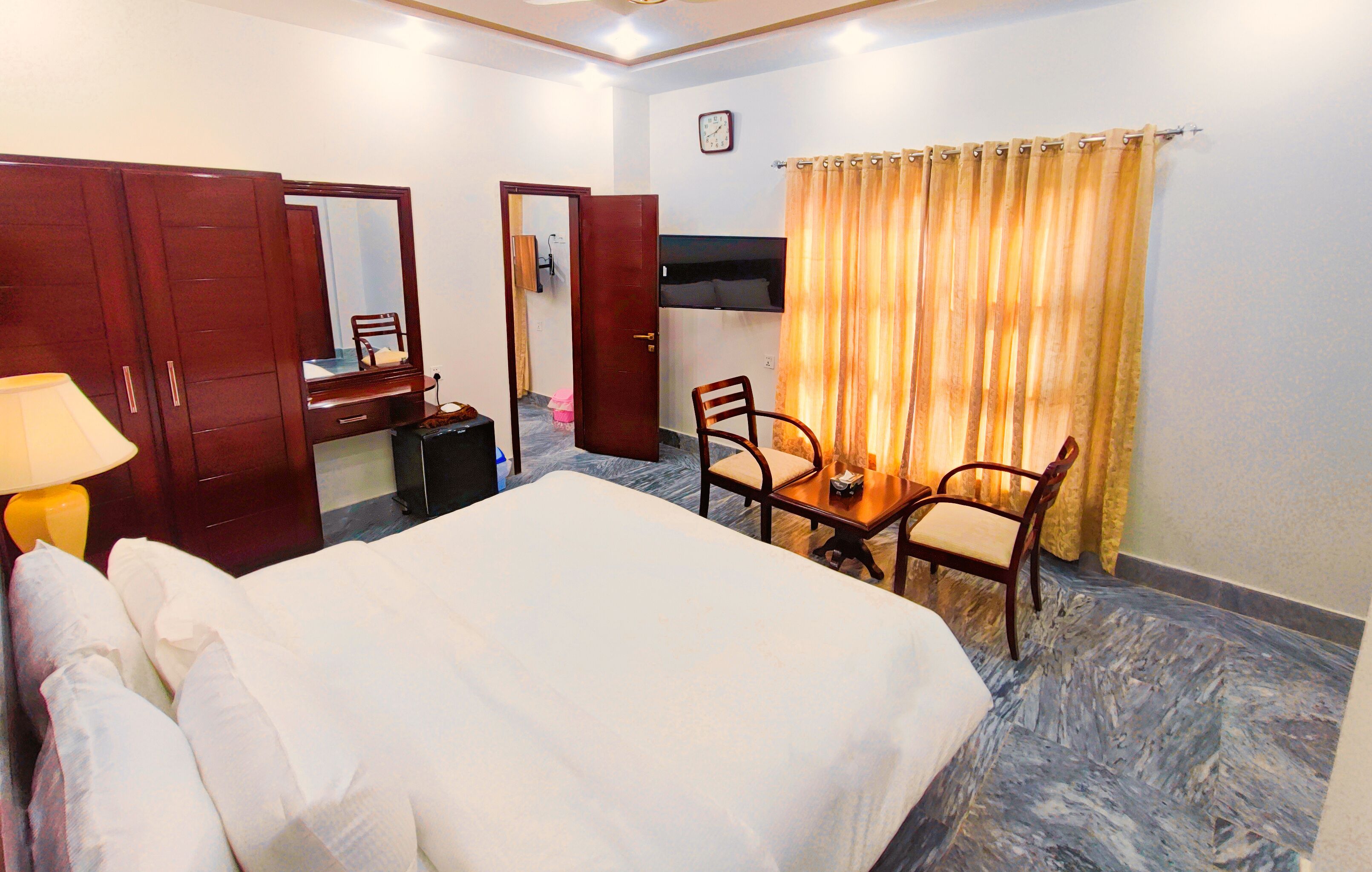 Una habitación de hotel con cama, escritorio, silla, espejo y televisor.