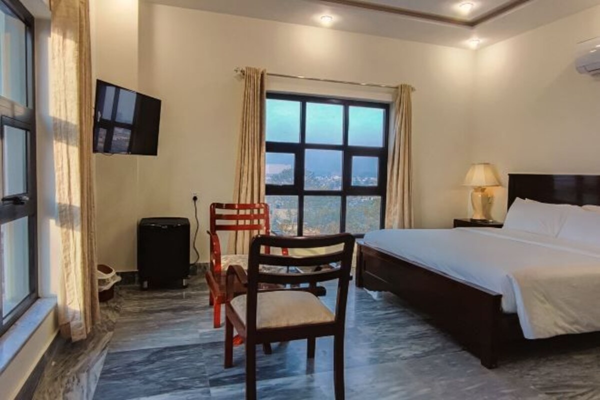 A hotel room with a bed, a TV mounted on the wall, a window with curtains, and a chair.