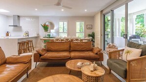 A modern living room with a brown leather sofa, wooden coffee table, and a dining area with a white table and chairs. - Sea La Vie - Port Douglas Villa (Port Douglas)