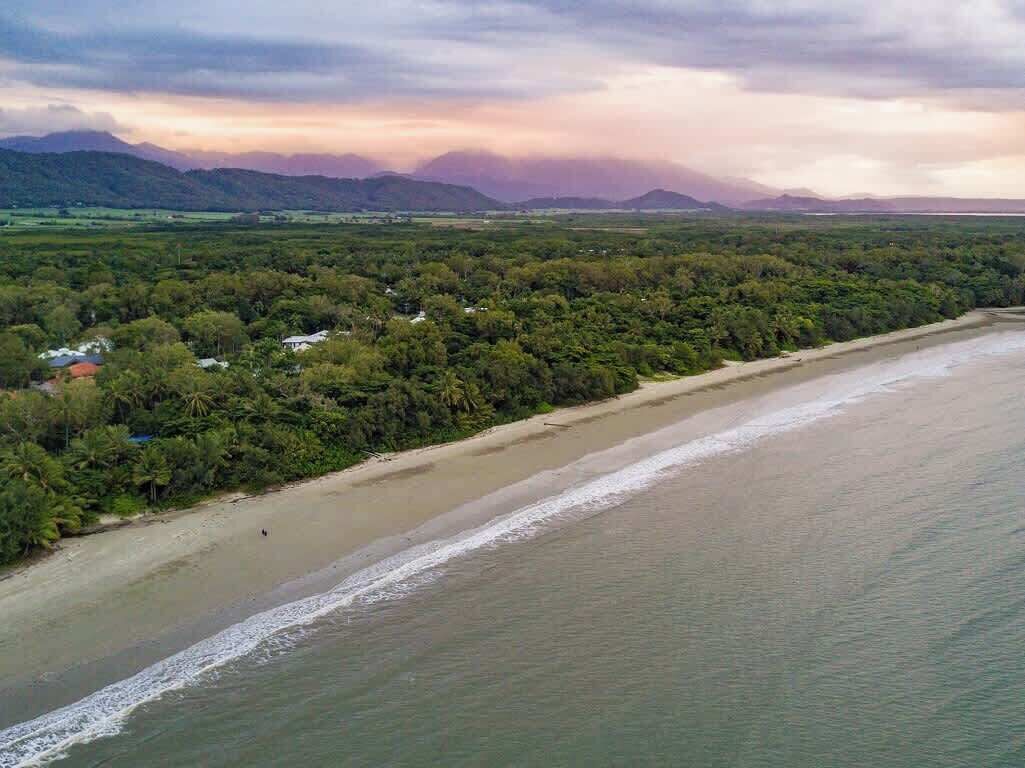 Un paisaje costero con playa, vegetación densa y montañas a lo lejos.