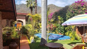 A patio with a round table and a lounge chair, a brick building, a swimming pool, and lush greenery. - Casita. W PRIVATE POOL (Ajijic)