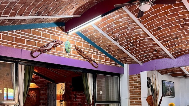 A cozy room with a brick ceiling, a purple accent wall, a sofa, and a dining table with a bottle of wine and decorative items. - Casita. W PRIVATE POOL (Ajijic)
