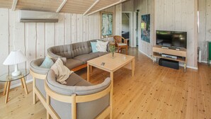 A modern living room with a wooden ceiling, a large sectional sofa, a coffee table, a TV stand, and a glass table with a lamp. - 3 bedroom lovely home in Samsø (Samsø)