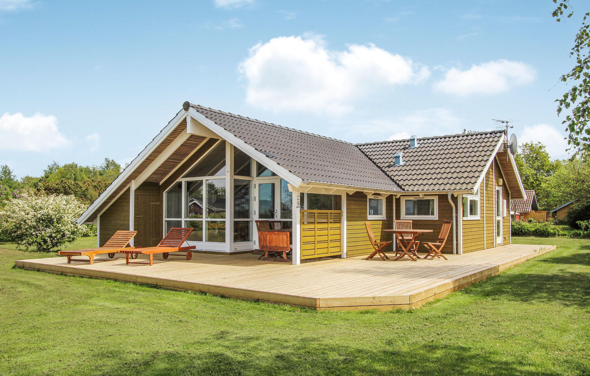Une maison moderne dotée d’une grande terrasse, de larges fenêtres et d’un toit en pente.
