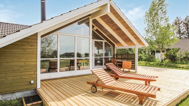 A modern house with a wooden deck, large sliding glass doors, and a covered patio area with two lounge chairs. - 3 bedroom lovely home in Samsø (Samsø)