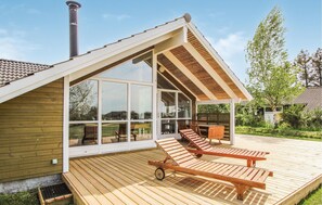 Une maison moderne dotée d’une terrasse en bois, de grandes portes-fenêtres coulissantes et d’un patio couvert avec deux fauteuils de relaxation.