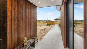Ein modernes Gebäude mit Holzfassade, Betondach und einem gepflasterten Weg, der zu einer Glastür führt.