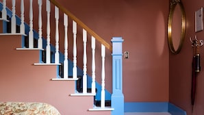 A staircase with white balusters and blue steps, a floral sofa with a patterned rug, and a herringbone-patterned floor.
