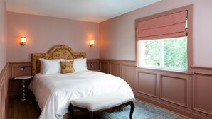 A bedroom with a large bed, two bedside tables, a window with a view, and wall sconces.