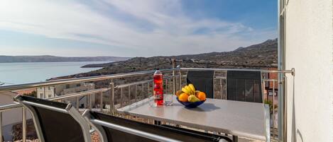 A balcony with a table, chairs, a bottle of ginger ale, and a bowl of fruit.