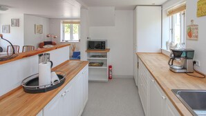 Uma cozinha compacta com armários brancos, bancada de madeira, micro-ondas, cafeteira e uma pequena estante com livros.