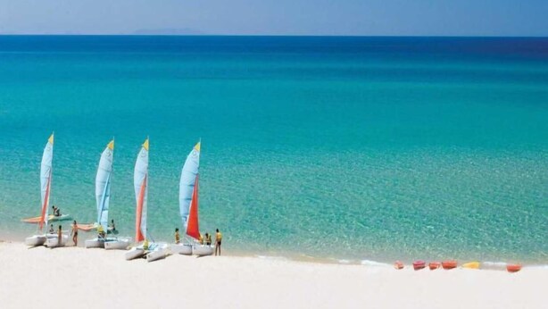 A beach with several sailboats lined up on the sand, a clear blue sea, and a few people in the water. - Apartment Emma by Interhome (Badesi)