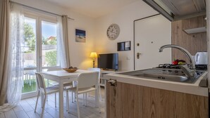 A modern kitchen with a built-in stove, a dining area with white chairs, a TV, and a clock on the wall. - Apartment Emma by Interhome (Badesi)