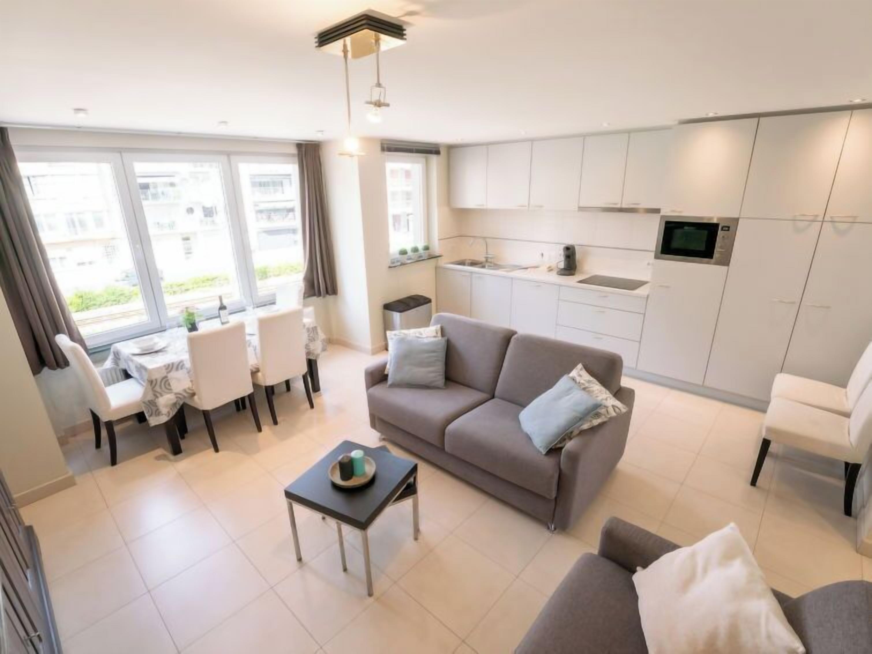 A modern apartment with a dining area, a sofa, a small table, and a kitchen with white cabinets and a microwave.