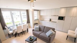 Een modern appartement met een eethoek, een bank, een kleine tafel en een keuken met witte kastjes en een magnetron.