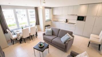 A modern apartment with a dining area, a sofa, a small table, and a kitchen with white cabinets and a microwave.