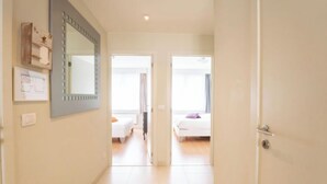 Een gang die leidt naar twee slaapkamers, met een grote spiegel aan de linker muur.