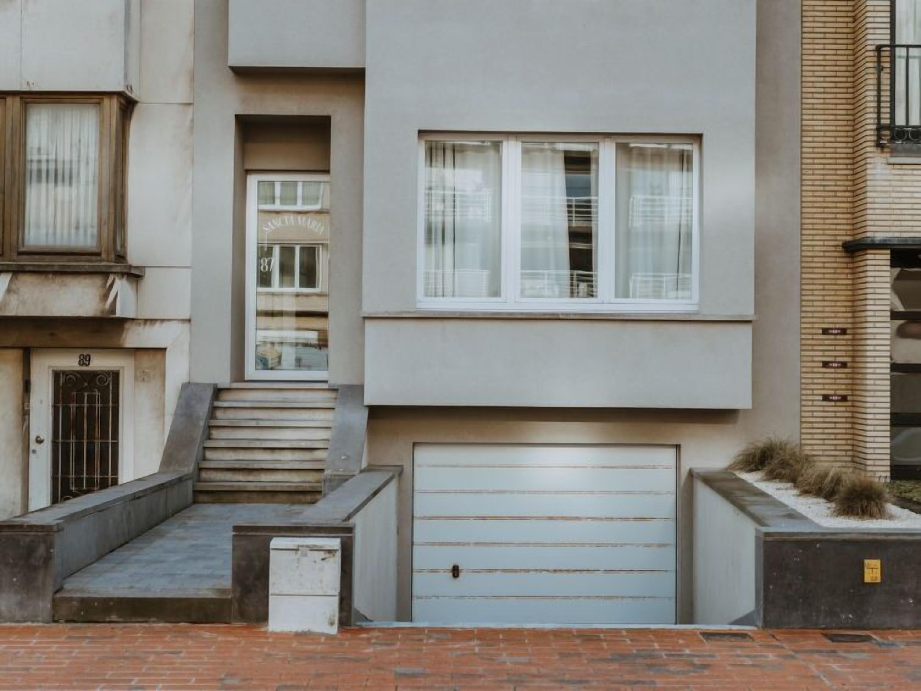A modern building with a flat facade, a central entrance with steps, and a garage door.