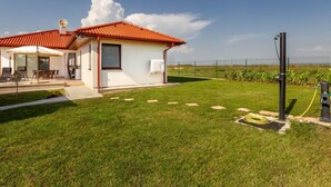 Une maison de plain-pied avec un toit recouvert de tuiles rouges, une terrasse avec des meubles d’extérieur et une pelouse bien entretenue.