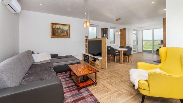 Un salon moderne avec un canapé, un fauteuil jaune et un coin repas comprenant une table et des chaises.