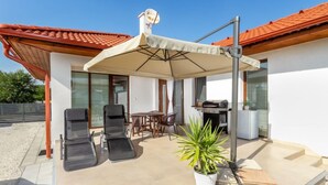 Un espace extérieur abrité, équipé d’une table et de chaises, d’un barbecue et d’une plante en pot.