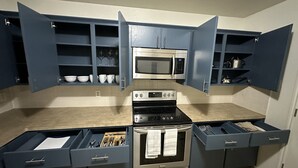 A kitchen with blue cabinets, a microwave, an oven, and a stovetop. - Zen space @ Harker Heights (Harker heigths)
