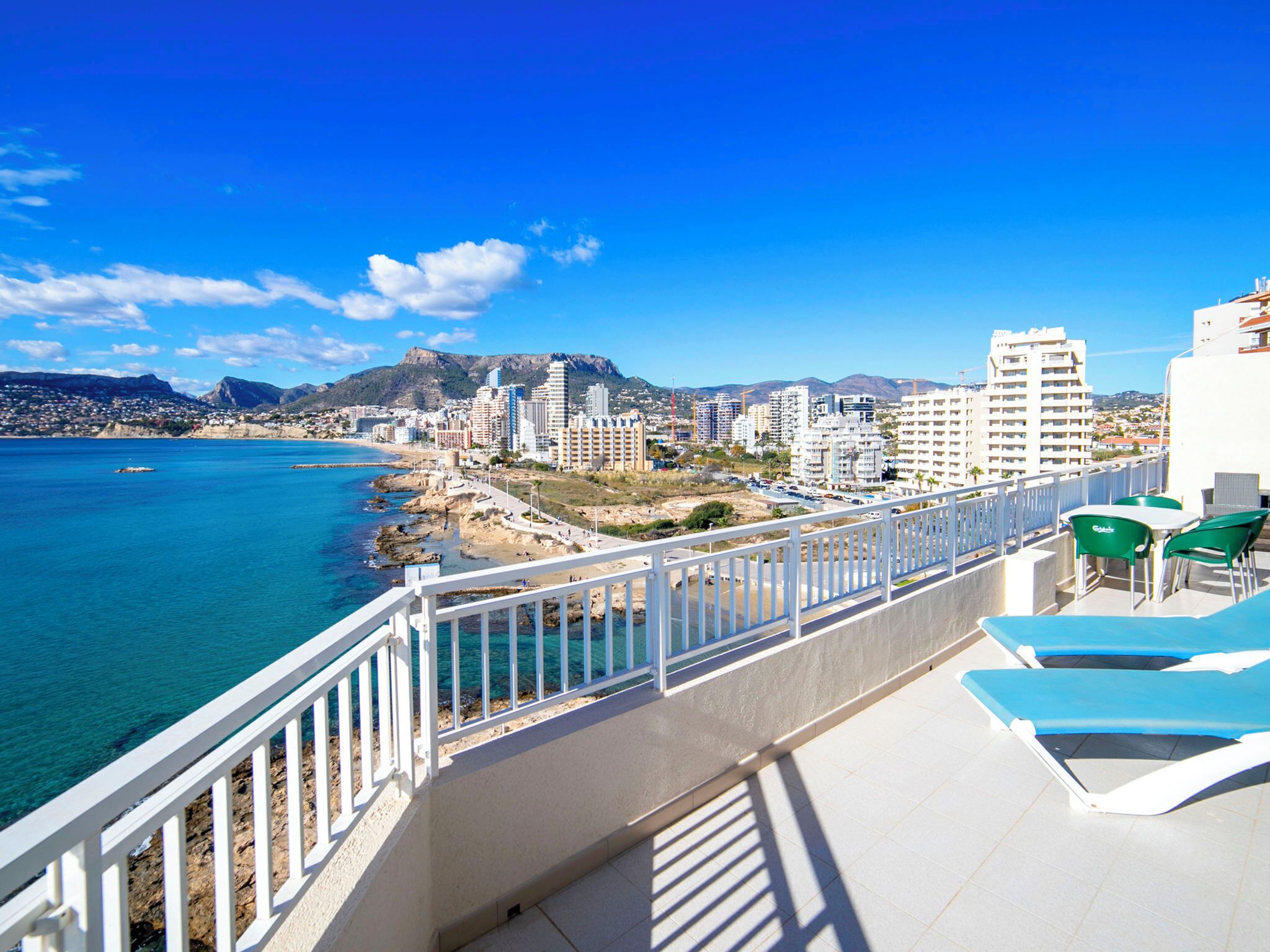 A balcony with a view of the sea and cityscape, including buildings and mountains.