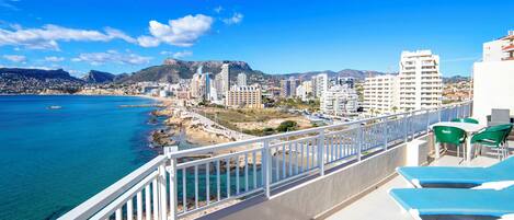 A balcony with a view of the sea and cityscape, including buildings and mountains.
