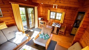 Interior acogedor de una cabaña de madera con sofá, sillones, una pequeña mesa de comedor y una zona de cocina.