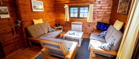 A cozy cabin interior with wooden walls, a sofa, a coffee table, and a television.