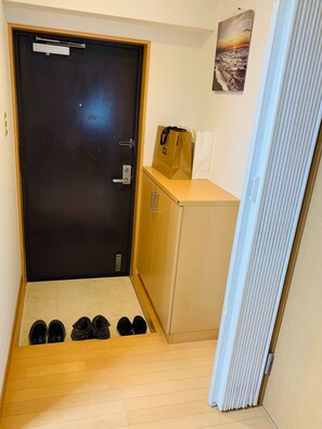 A room with a door, a small cabinet, a pair of shoes, and a bag on the floor.