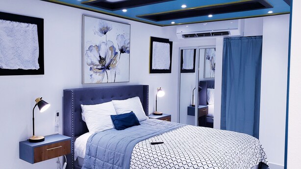 Une chambre à coucher moderne avec un grand lit, des lampes de chevet, un luminaire au plafond et des œuvres d’art accrochées aux murs.