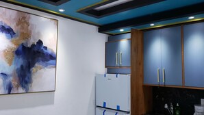 Une cuisine moderne avec des meubles bleus, un réfrigérateur blanc et un grand tableau abstrait accroché au mur.