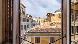 Vista a través de una ventana con marco de metal, que da a una calle con edificios y tejados de tejas.