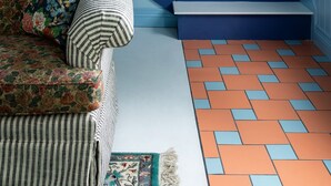 A living room with a blue staircase, a floral sofa, a striped armchair, and a patterned rug.