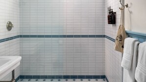 A bathroom with white and blue tiles, a shower, a sink, and a towel rack.
