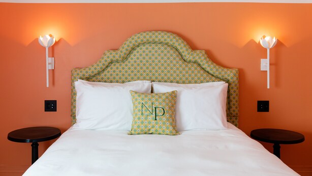 A neatly made bed with white linens, a patterned pillow, and a headboard with a geometric design. There are two small round tables beside the bed.