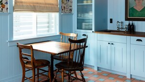 A kitchen with a wooden table and chairs, a window with blinds, and a wall with floral wallpaper.