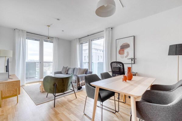 Uma sala de estar moderna com uma mesa de madeira, cadeiras cinzas, uma poltrona verde e um sofá.