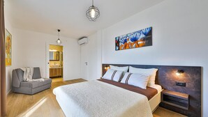 Una camera da letto moderna con un grande letto, una poltrona grigia, un quadro e un design di testiera originale.
