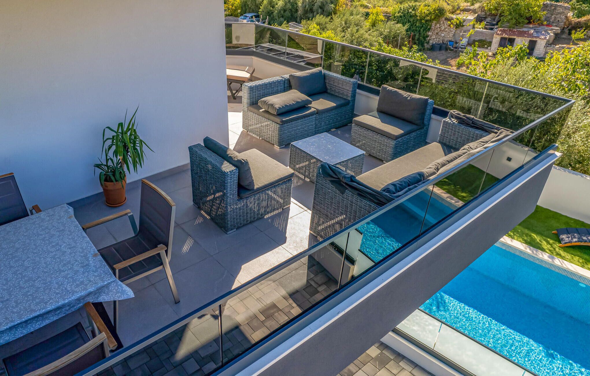 A modern outdoor balcony with a glass railing, wicker furniture, a small table, and a potted plant.