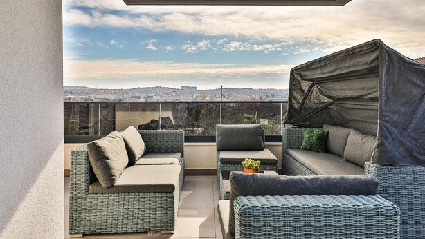 Un balcone con mobili in vimini, un tavolino con una pianta e vista sulla città.