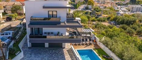 A modern multi-story house with a rooftop pool and a view of the surrounding area.