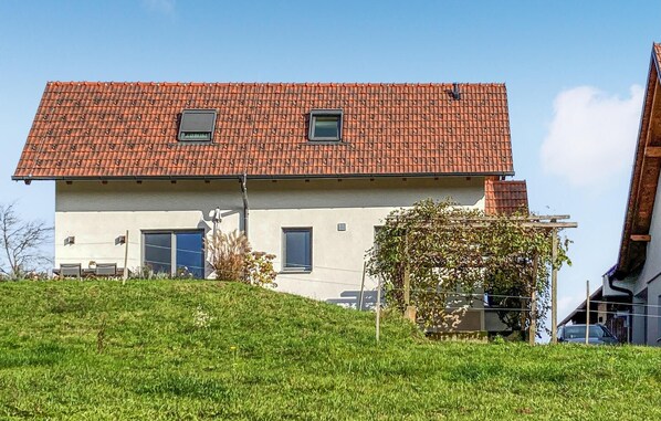 Une maison à deux étages, avec un toit recouvert de tuiles rouges, une petite fenêtre à l’étage supérieur et une porte de garage au rez-de-chaussée.