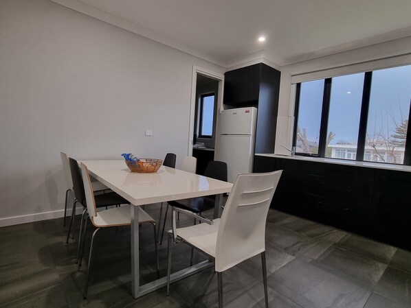 A modern kitchen with a white table and chairs, a black refrigerator, and a window with a view. - New spacious modern apartment in St Kilda (St Kilda East)