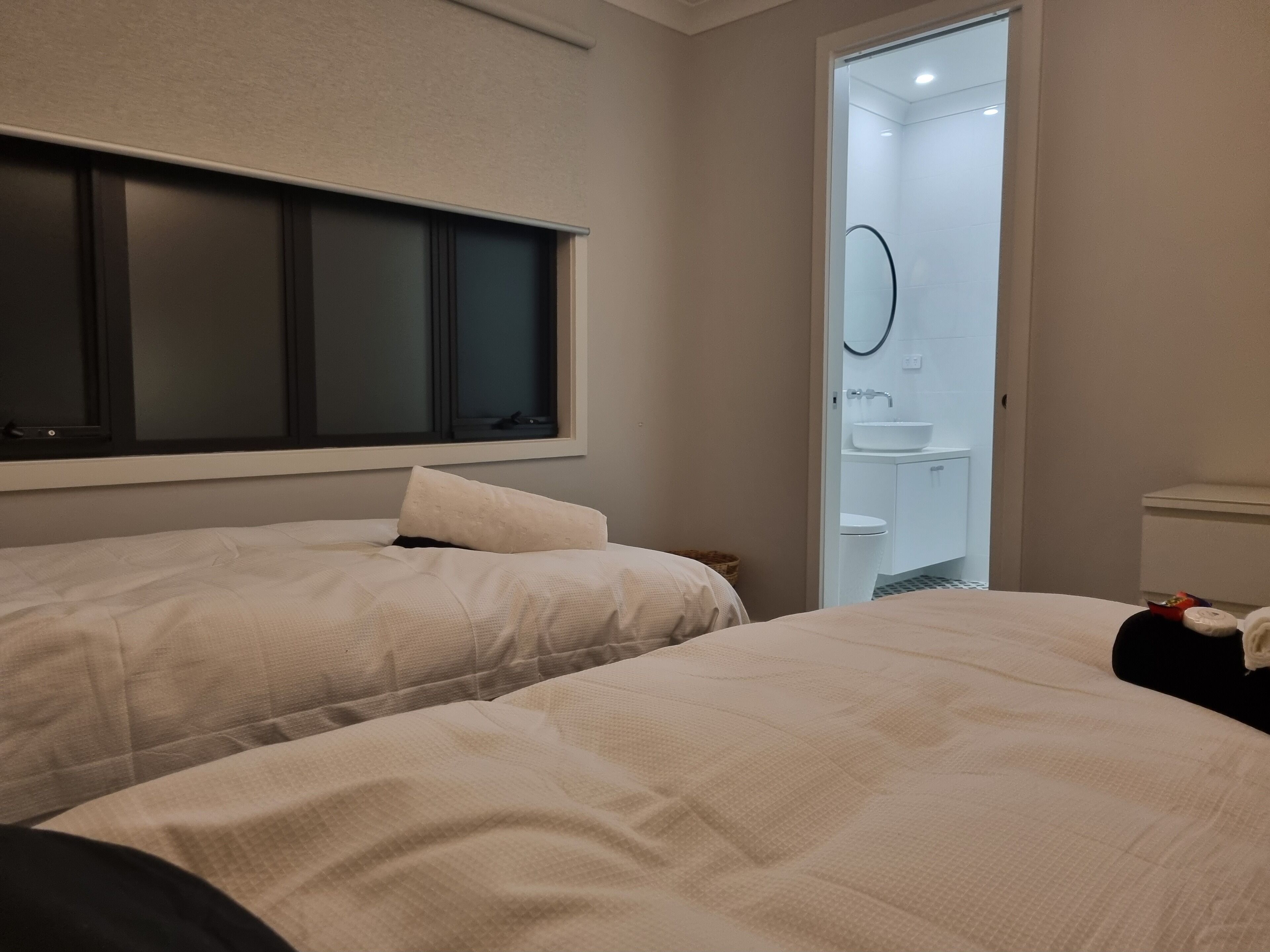 Habitación de hotel con dos camas, un ventanal amplio y un baño visible a través de una puerta abierta.