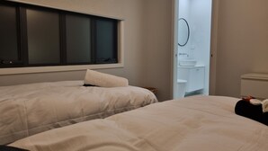 Habitación de hotel con dos camas, un ventanal amplio y un baño visible a través de una puerta abierta.