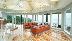 Un salón amplio con suelo de madera, ventanas grandes y vistas al exterior.