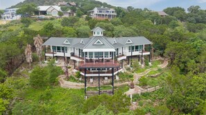 A modern multi-story house with a central tower, surrounded by lush greenery and a winding path.